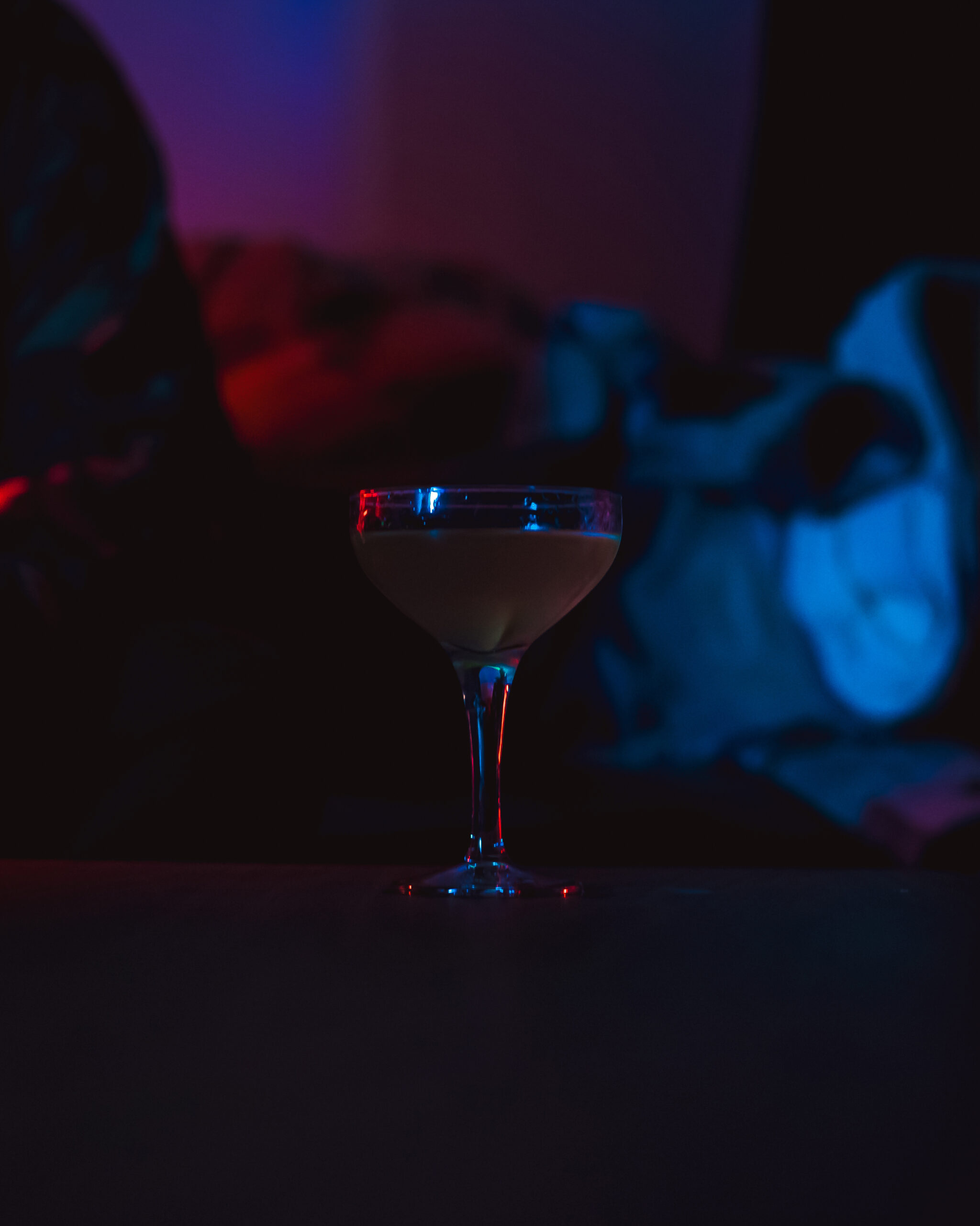 A "50/50 Martini" is elegantly presented in a cocktail glass, illuminated by moody blue and red lighting.