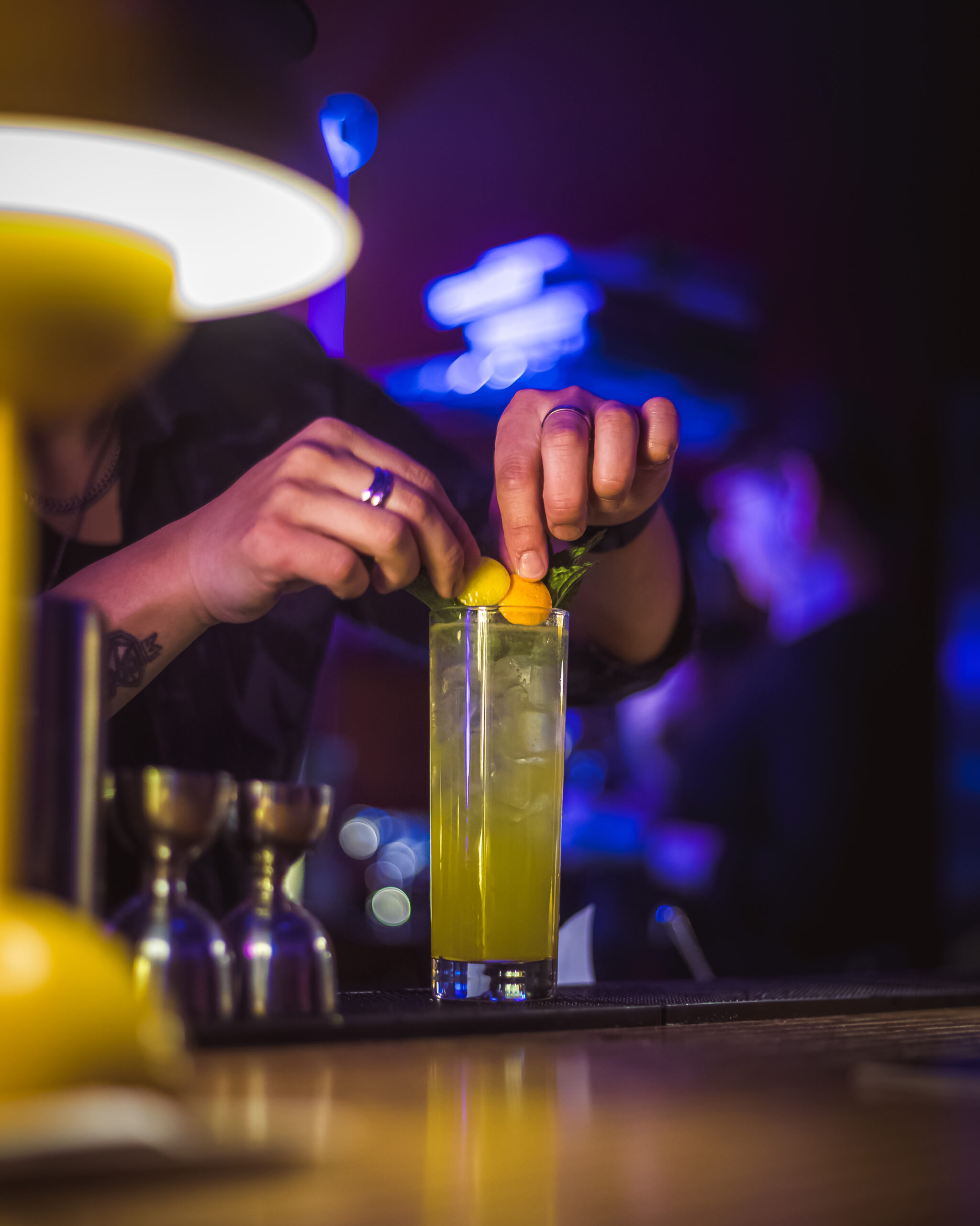 Bartender garnishing a Harvey Wallbanger cocktail with orange slices and mint at a dimly lit bar.