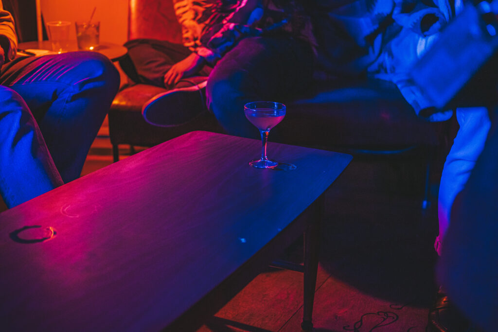 A cocktail glass on a table under colorful lighting at the "Play It Cool Pop-Up Bar Event."