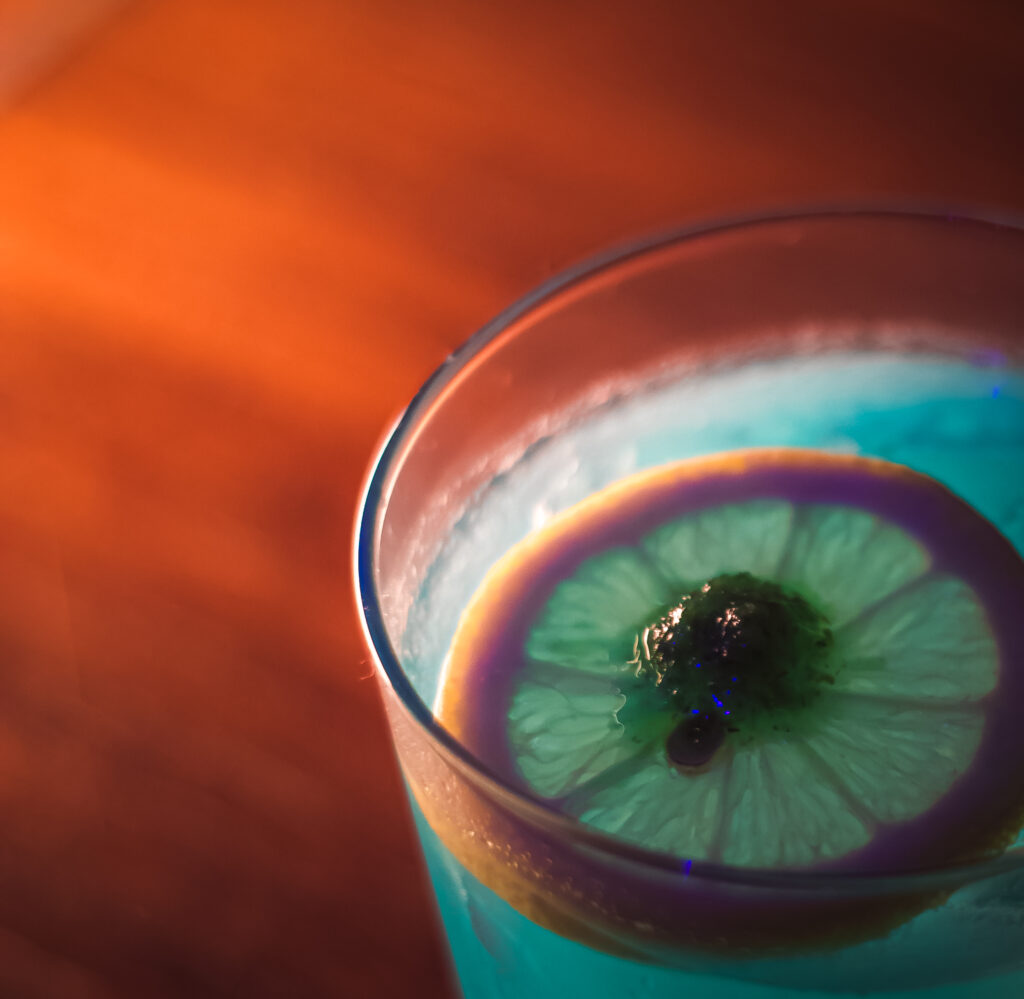 A vibrant blue cocktail with a slice of lemon and a cherry, featured at the "Play It Cool Pop-Up Bar Event."