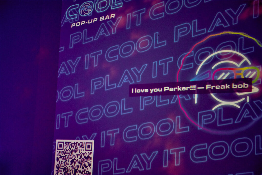 Colorful wall with "PLAY IT COOL" text and a message: "I love you Parker!!! — Freak bob." QR code visible.