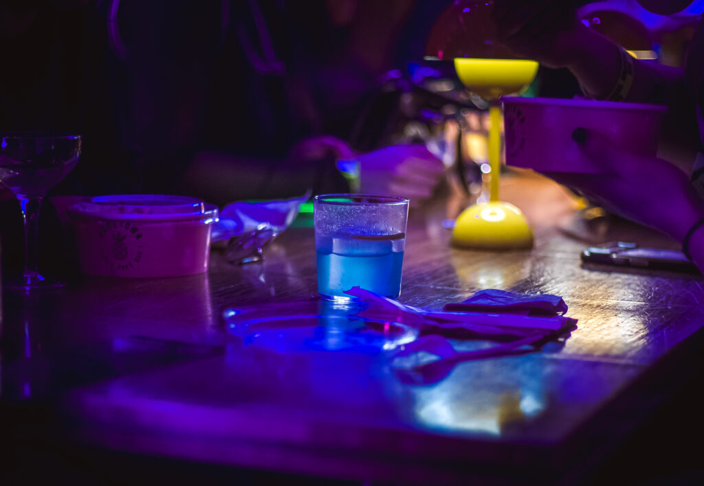 Craft Cocktail Play It Cool Pop-Up Bar Event with a glowing blue drink and colorful neon lighting on a wooden bar.