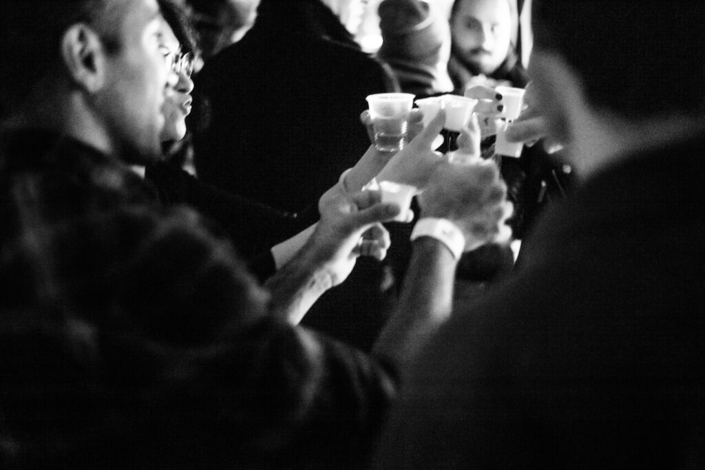 People raising glasses in a toast at the "Play It Cool Pop-Up Bar Event," captured in black and white.