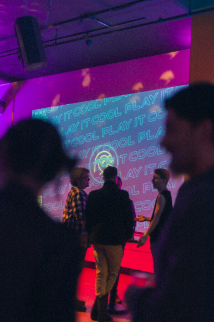 "Play It Cool Interactive Audio Visualizer" projected on a wall, with people conversing in a dimly lit room.