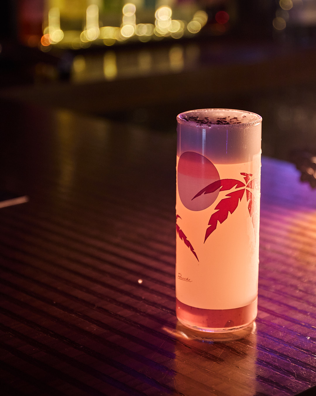 A tall glass of gin fizz with a decorative design sits on a dimly lit bar.